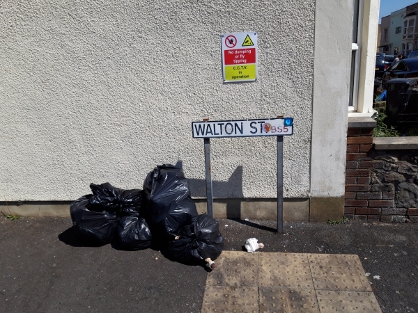 Photo shows fly-tipping beneath sign advising no fly-tipping, CCTV in operation