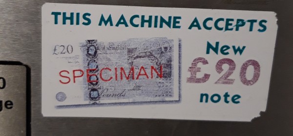 Sticker on machine stating this machine accepts new £20 note. On the image of the note is the printed word SPECIMAN.