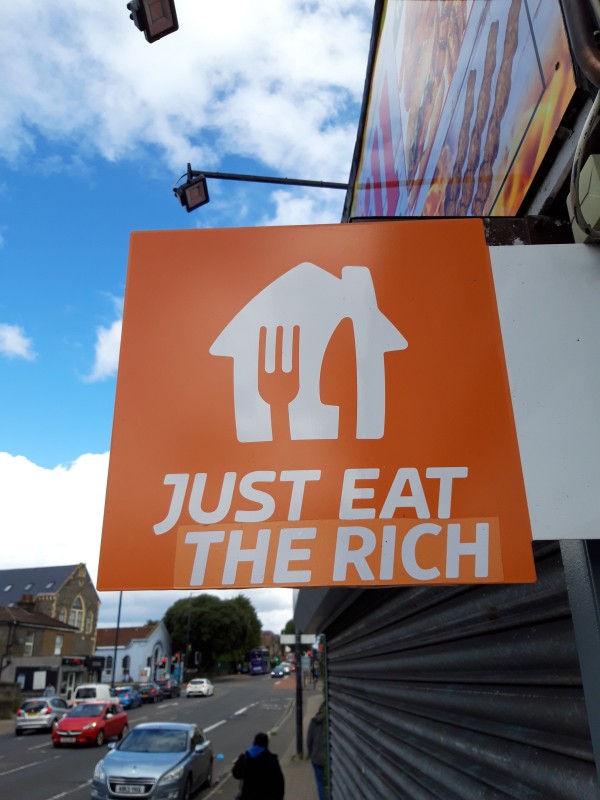 Subvertised sign on disused takeaway now reading Just Eat The Rich