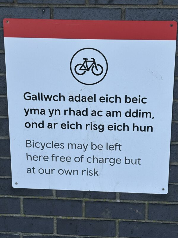 Welsh text = You can leave your bike here for free, but at your own risk. English text - Bicycles may be left here free of charge but at our risk