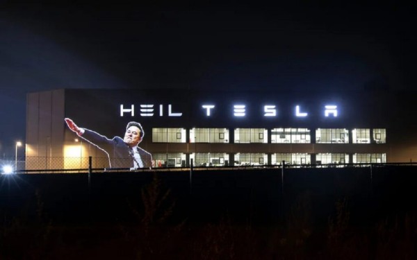 Next to Tesla illuminated sign, a projection with the word Heil and a picture of Musk giving a fascist salute