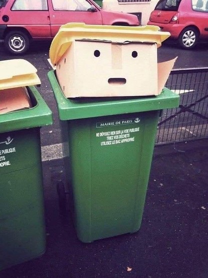 Parisian dustbin topped with a cardboard box sporting the distinctive Trump haircut